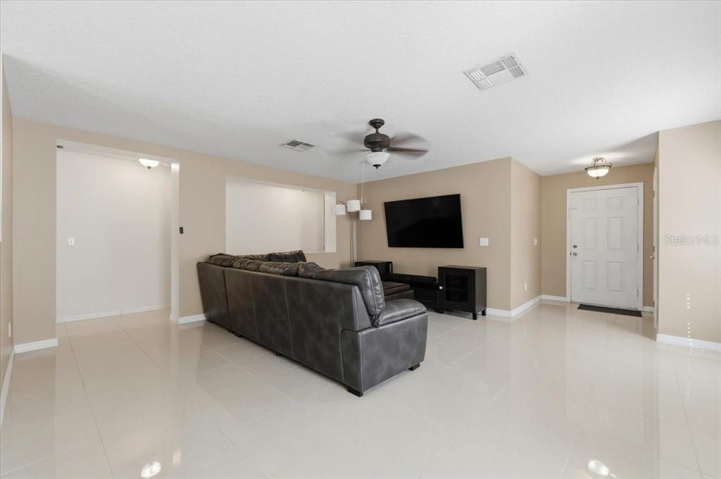 A living room features a grey sectional sofa, a wall-mounted television, and light tile flooring — 14852 PELLICER DRIVE, ORLANDO, FL