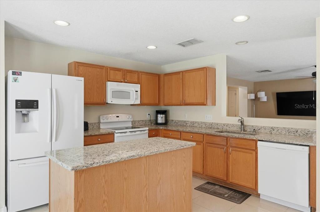 A kitchen features wood cabinets, granite countertops, a kitchen island, and white appliances — 14852 PELLICER DRIVE, ORLANDO, FL