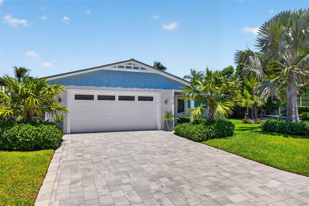 A blue-sided house with a white garage door and a paved driveway under a sky — 819 59TH AVENUE, ST PETE BEACH, FL