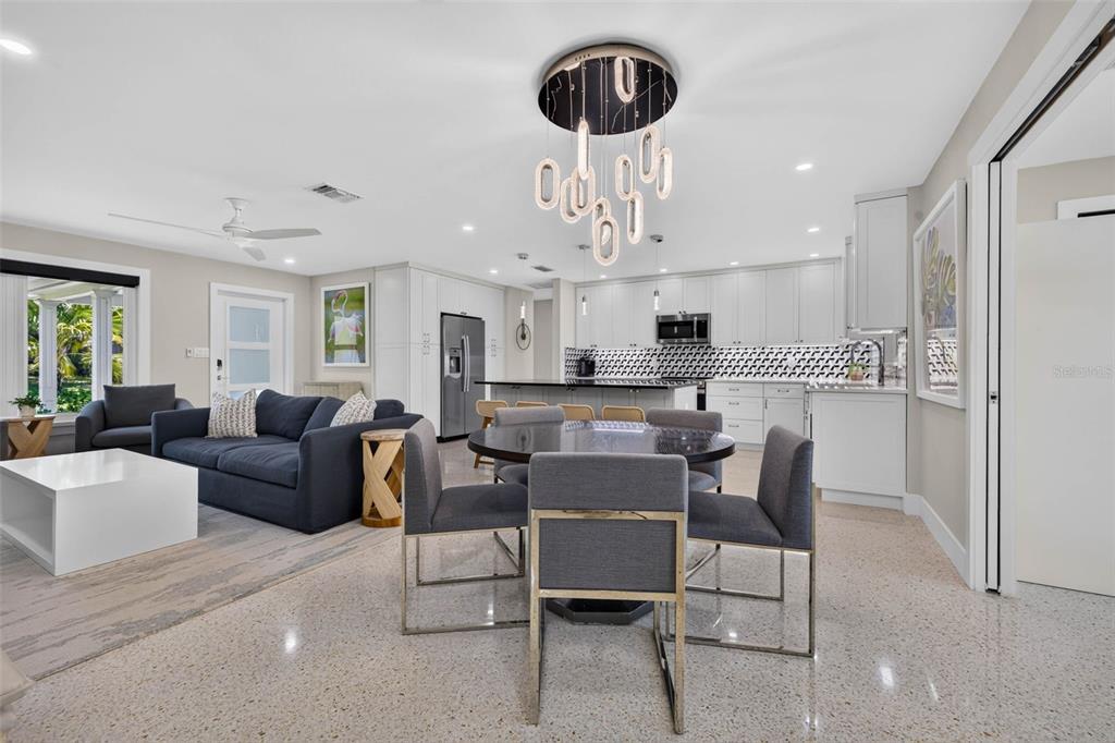 An open-concept living and dining area features a modern chandelier, white cabinetry, and terrazzo flooring — 819 59TH AVENUE, ST PETE BEACH, FL