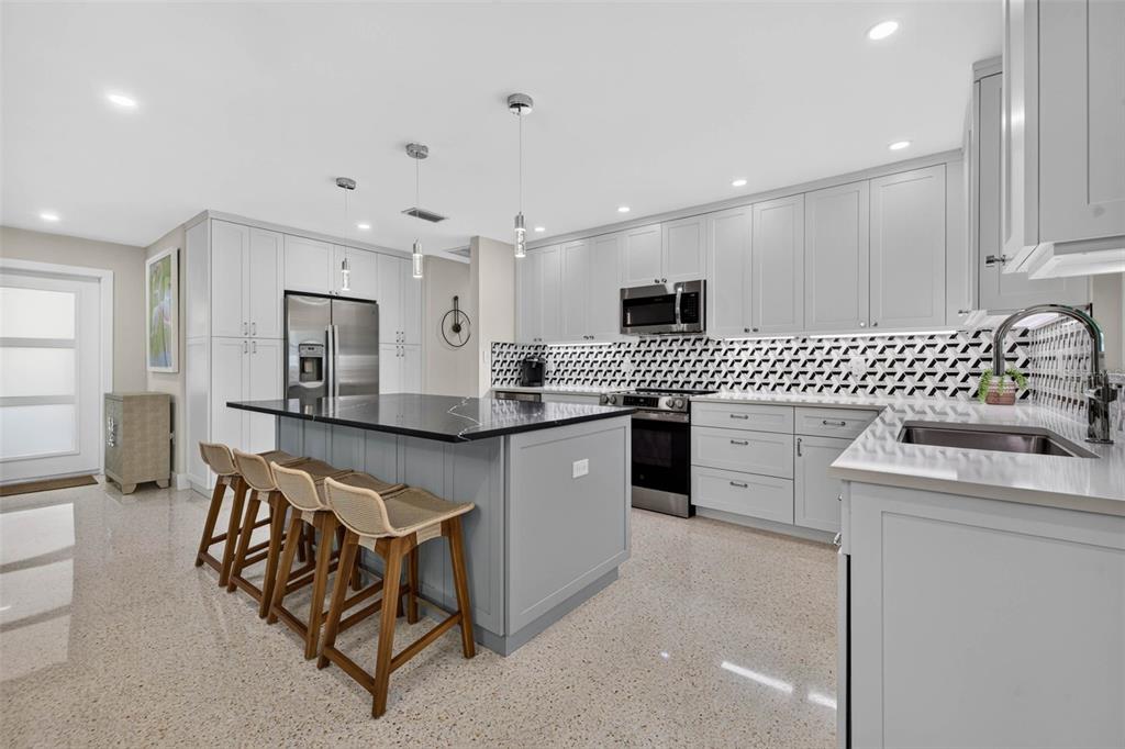 A modern kitchen features light gray cabinets, a black-topped island, and a patterned tile backsplash — 819 59TH AVENUE, ST PETE BEACH, FL