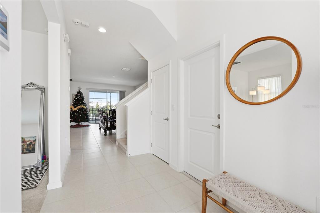 A bright entryway features white walls, tile flooring, two closed doors, and a round mirror — 4454 MONADO DRIVE, KISSIMMEE, FL