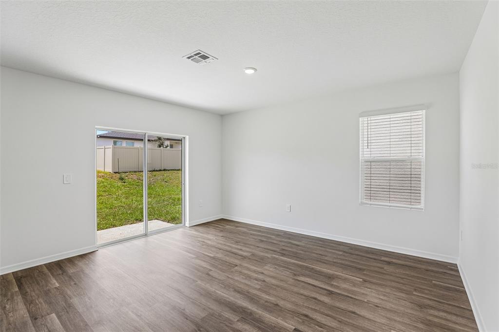 An empty room with white walls, wood-look flooring, a sliding glass door, and one window — 5373 WILLOW CREEK, HAINES CITY, FL