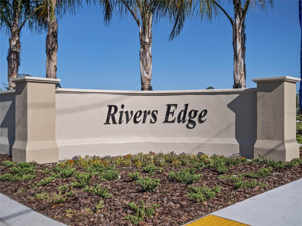 A beige monument sign with the text Rivers Edge stands in front of palm trees — 2704 GOLDEN TROUT LANE, EDGEWATER, FL