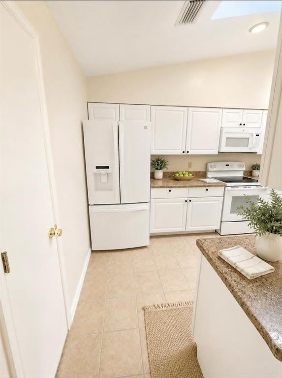 A kitchen features white cabinetry, a white refrigerator, a white stove, and tan tile flooring — 1203 SAXONY CIRCLE UNIT C, PUNTA GORDA, FL