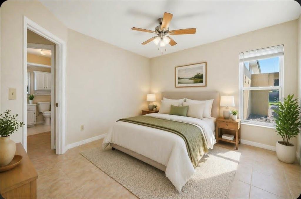 A bedroom with a queen bed, ceiling fan, tile floors, and an attached bathroom — 1203 SAXONY CIRCLE UNIT C, PUNTA GORDA, FL