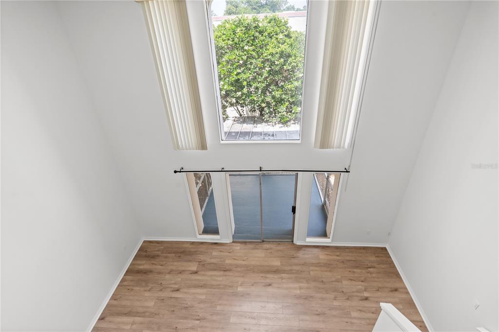 A high-angle view of a living room with wood-look flooring, tall windows, and sliding doors — 500 ORANGE DRIVE UNIT 10, ALTAMONTE SPRINGS, FL