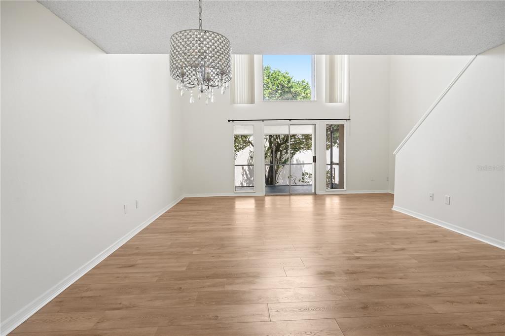 A living room with light wood flooring, a crystal chandelier, and large sliding glass doors — 500 ORANGE DRIVE UNIT 10, ALTAMONTE SPRINGS, FL