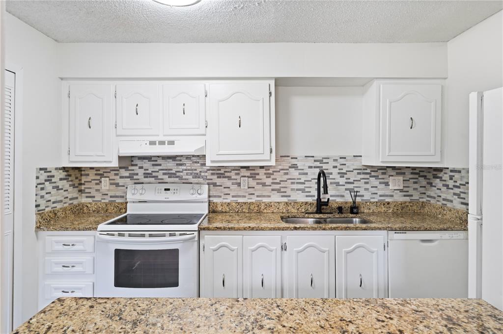 A kitchen features white cabinets, granite countertops, a tiled backsplash, and white appliances — 500 ORANGE DRIVE UNIT 10, ALTAMONTE SPRINGS, FL