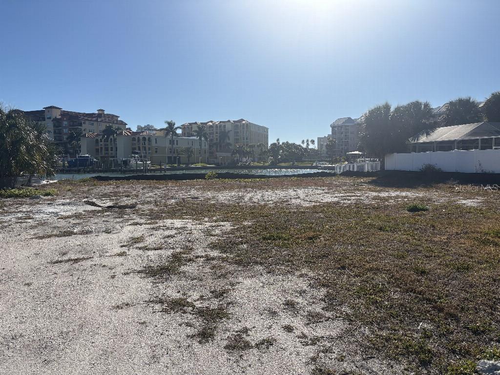 A vacant, sandy waterfront lot faces a canal with multi-story residential buildings in the background — 5410 ALOHA DRIVE, ST PETE BEACH, FL