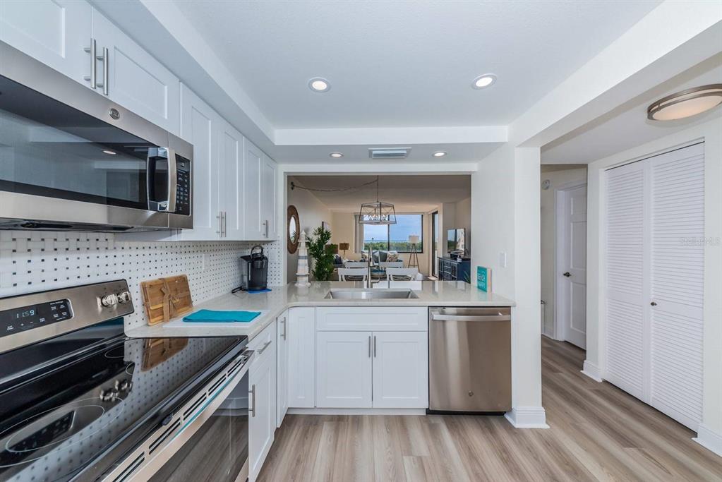 A modern kitchen features white cabinets, stainless steel appliances, and a view into the living area — 6357 BAHIA DEL MAR BOULEVARD UNIT 407, ST PETERSBURG, FL