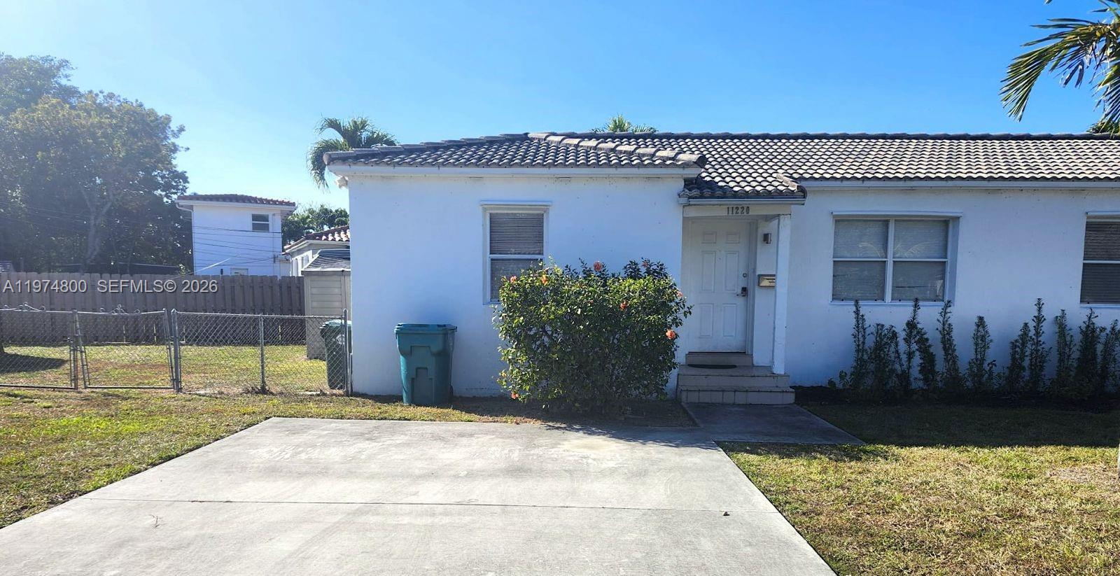 A single-story white house features a concrete driveway, a front door, and a fenced yard — 11220 NE 11th Pl # 11220, Biscayne Park FL 33161, BISCAYNE PARK, FL