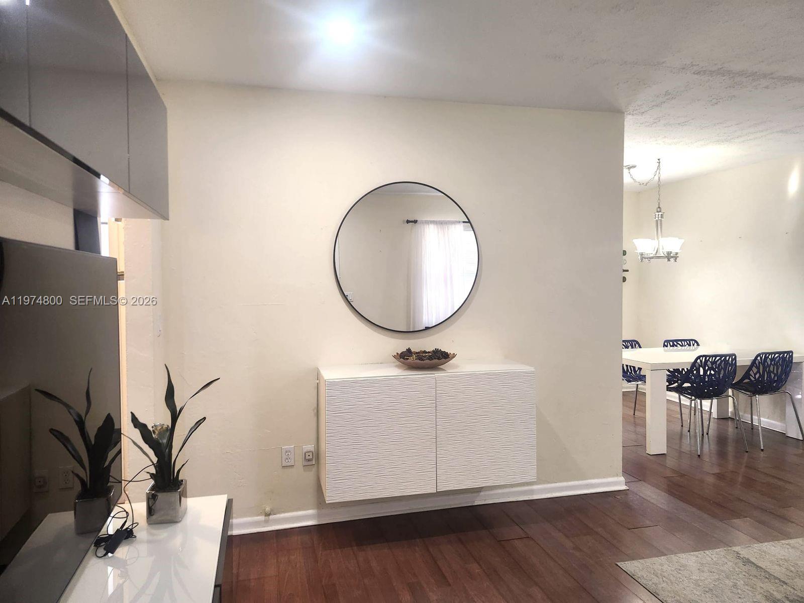 A white wall features a round mirror above a floating cabinet with dark wood flooring — 11220 NE 11th Pl # 11220, Biscayne Park FL 33161, BISCAYNE PARK, FL