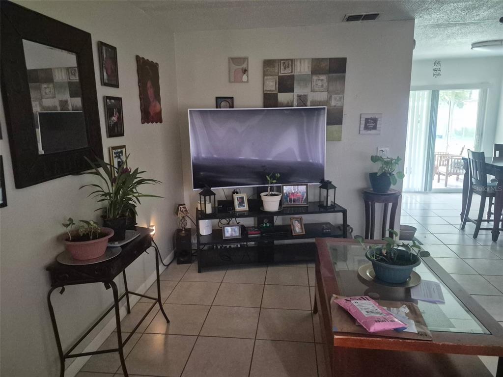A living room features a large television on a black stand, tile flooring, and decor — 723 24TH STREET NW, WINTER HAVEN, FL
