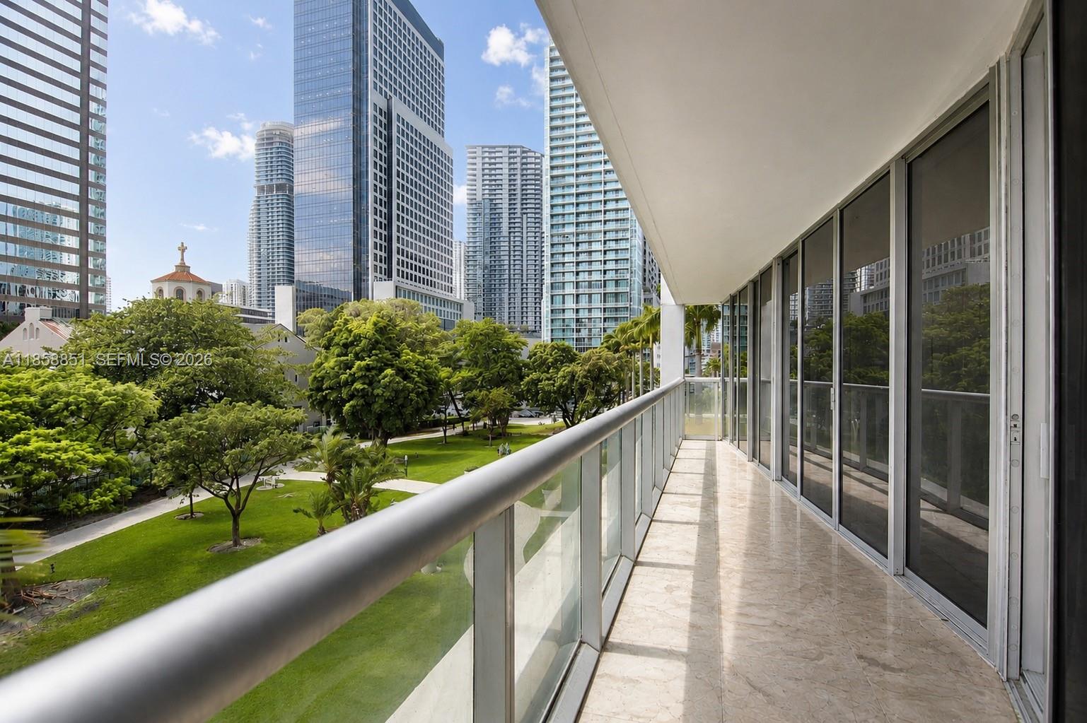 A balcony with a glass railing overlooks a park and city skyline — 495 Brickell Ave # 411, Miami FL 33131, MIAMI, FL