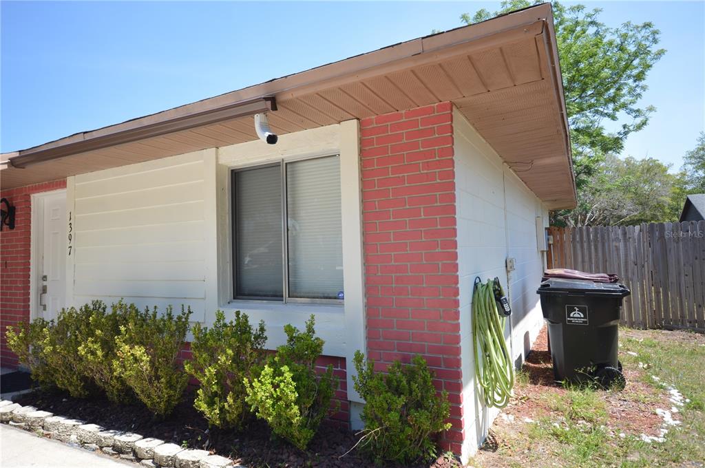 A side view of a house exterior featuring red brick, white siding, and a window — 1397 CANDLEWYCK DRIVE, ORLANDO, FL