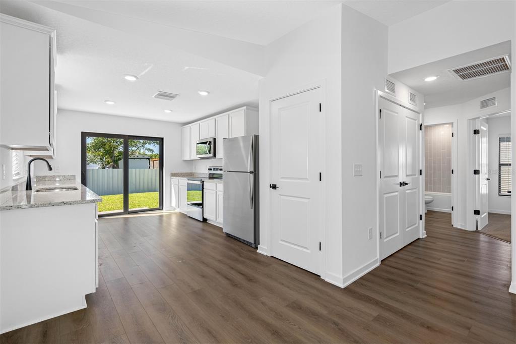 A kitchen with white cabinets, stainless steel appliances, and wood-look flooring leads to a patio — 602 BLACKTHORN DRIVE, LAKELAND, FL