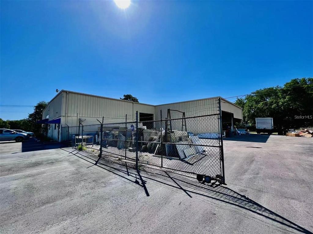 A fenced-in industrial building exterior with a paved parking lot under a clear blue sky — 2398 63RD AVENUE E, BRADENTON, FL