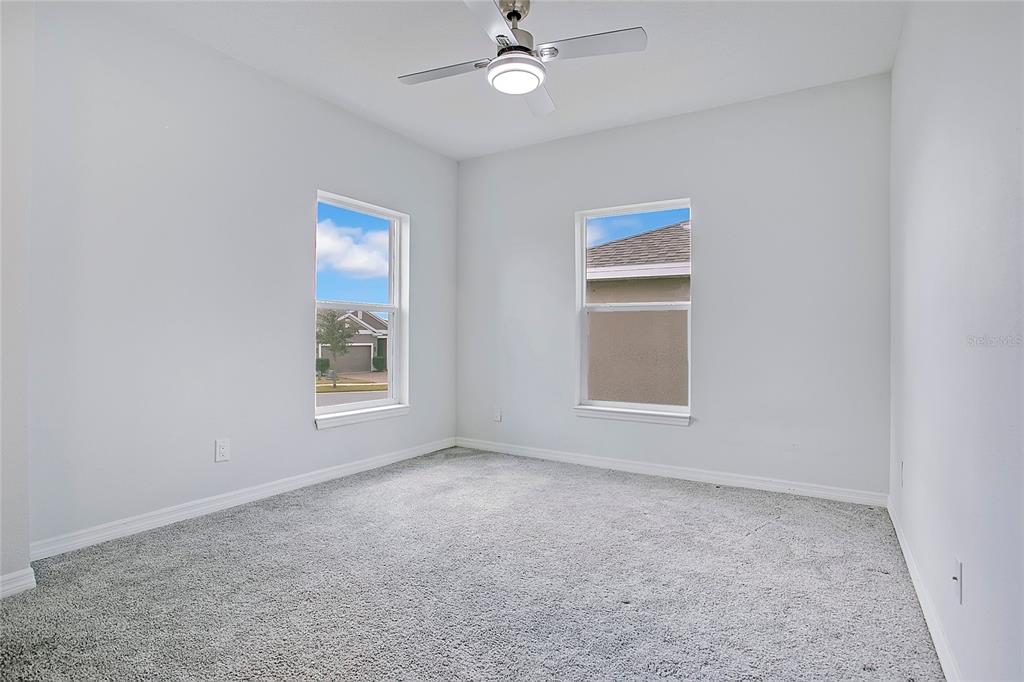An empty bedroom features gray carpet, white walls, two windows, and a ceiling fan — 427 IRONSIDE TRAIL DRIVE, GROVELAND, FL