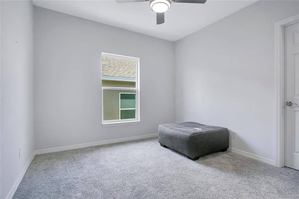 A bedroom with light gray walls, gray carpet, a ceiling fan, and a gray ottoman — 427 IRONSIDE TRAIL DRIVE, GROVELAND, FL