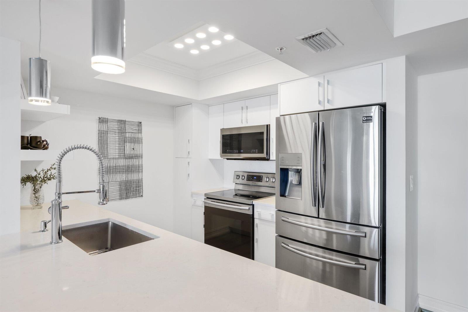 A modern kitchen features white cabinets, stainless steel appliances, and a quartz countertop island — 99 SE Mizner Boulevard # 609, Boca Raton FL 33432, BOCA RATON, FL