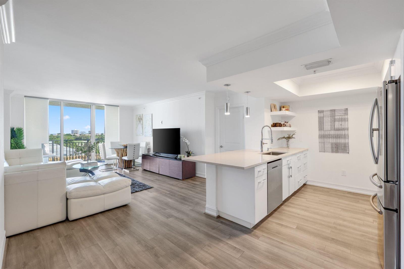 An open-concept living area with a white kitchen island, stainless appliances, and wood-look flooring — 99 SE Mizner Boulevard # 609, Boca Raton FL 33432, BOCA RATON, FL