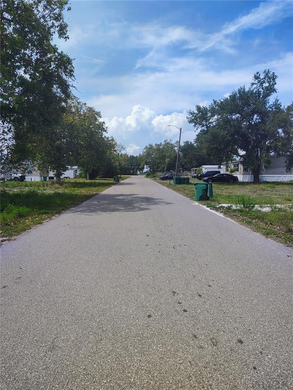 A paved residential street lined with trees, grass, and mobile homes under a blue sky — 9315 MANDY STREET, PUNTA GORDA, FL