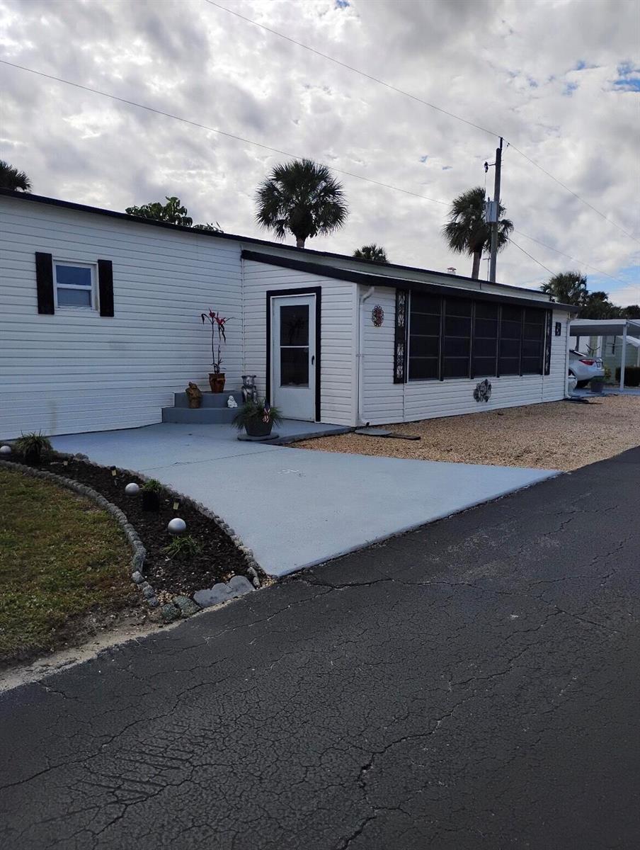 A white mobile home with a gray concrete driveway, a screened porch, and palm trees — 13827 S Indian River Drive # 5, Jensen Beach FL 34957, JENSEN BEACH, FL