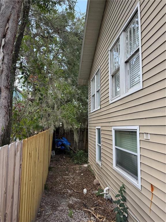 A narrow side yard between a tan vinyl-sided house and a wooden privacy fence — 610 21ST STREET W, BRADENTON, FL