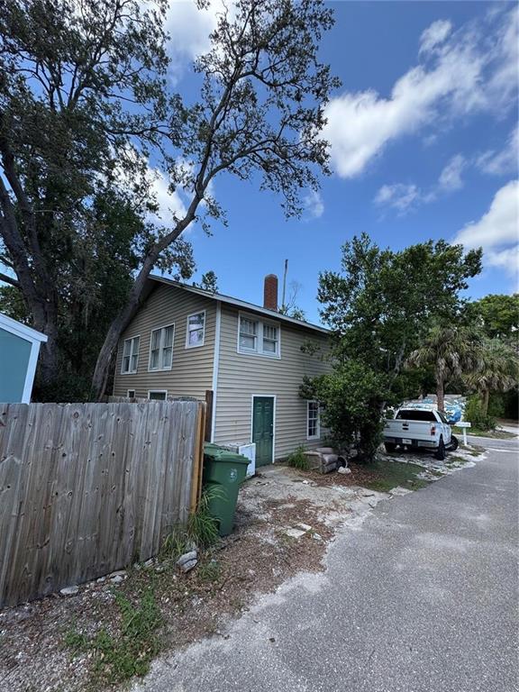 A two-story house with tan siding, a chimney, and a green door sits near a road — 610 21ST STREET W, BRADENTON, FL