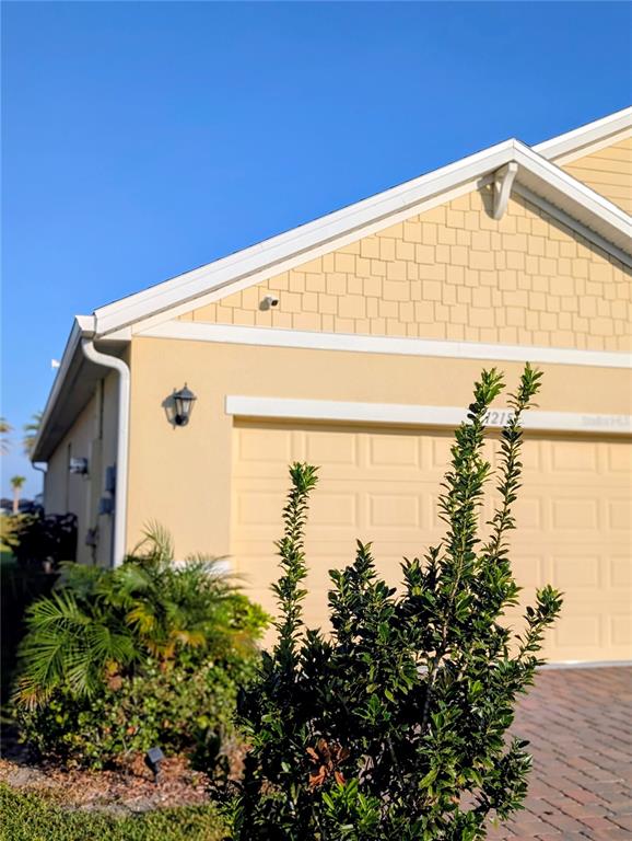 A yellow house exterior features a garage, a wall-mounted light, and a prominent green shrub — 1215 DUGAN CIRCLE SE, PALM BAY, FL