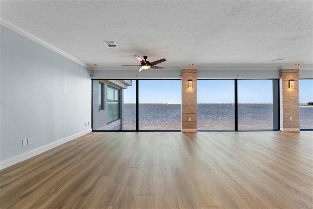An empty living room features wood-look flooring, a ceiling fan, and large windows overlooking water — 1600 W MARION AVENUE UNIT 234, PUNTA GORDA, FL