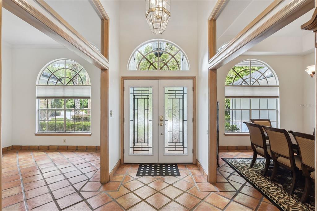An entryway with terracotta tile floors, double glass-paneled doors, and arched windows on both sides — 381 CREEKSTONE COURT, LONGWOOD, FL