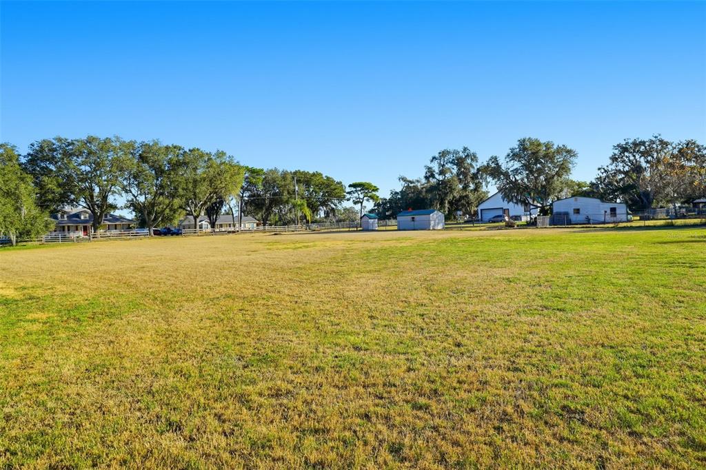 A large, grassy field with scattered trees and several small buildings in the background — 7005 CRIPPLE CREEK ROAD, PLANT CITY, FL