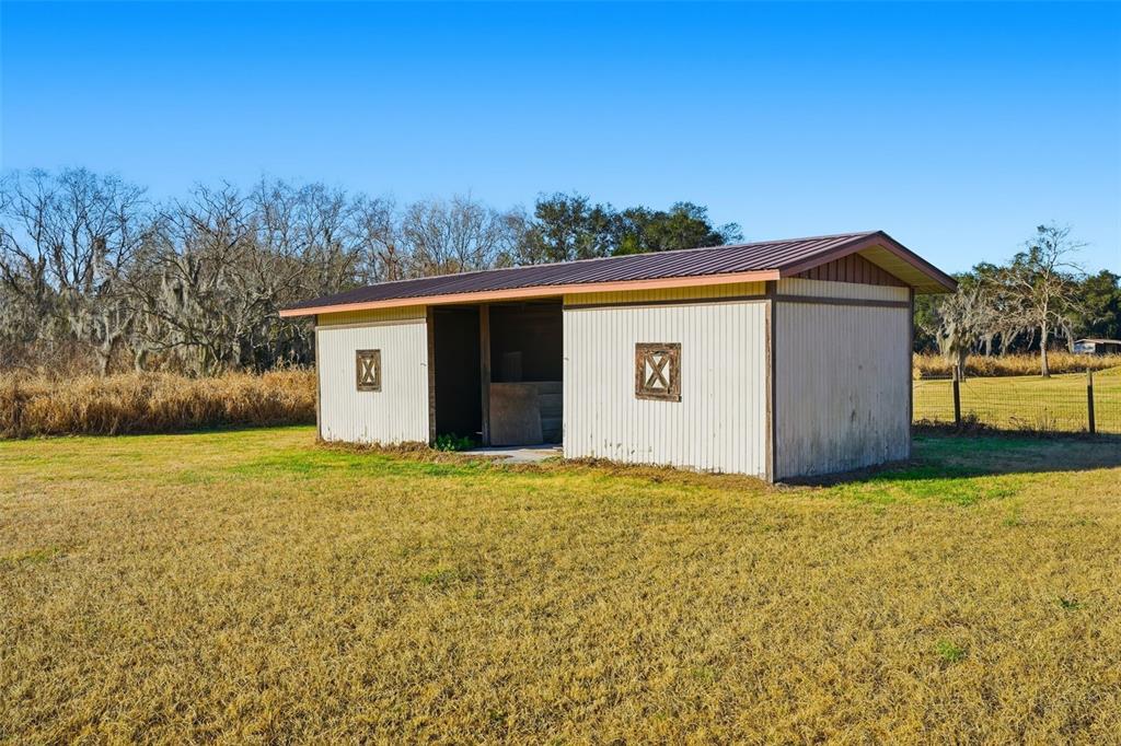 A small, light-colored wooden shed with a metal roof sits in a grassy field — 7005 CRIPPLE CREEK ROAD, PLANT CITY, FL