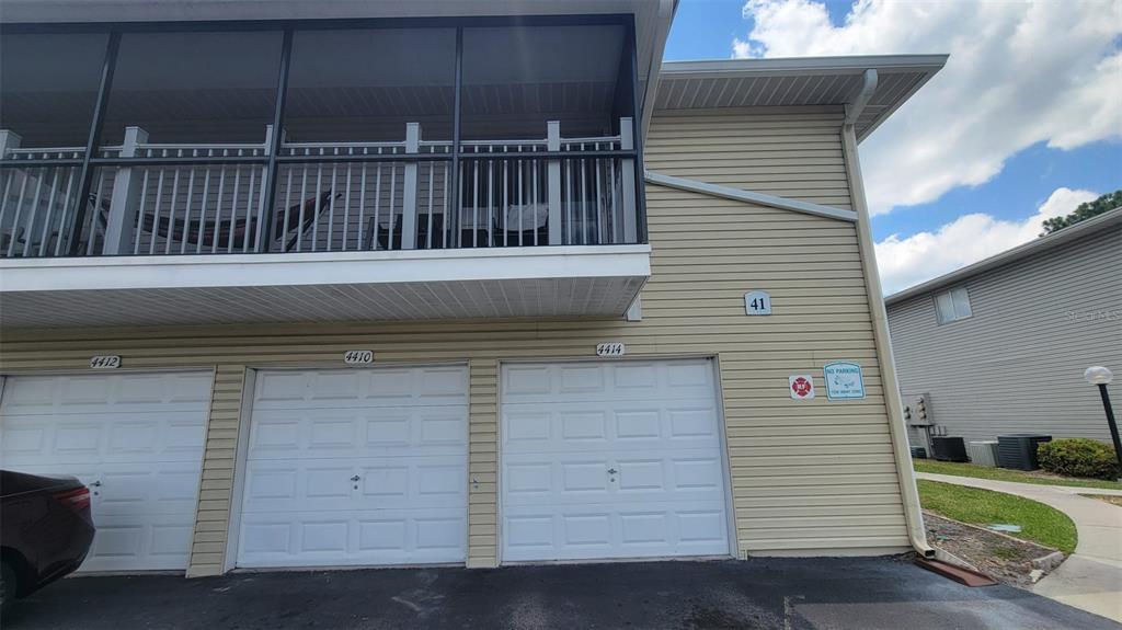 A two-story building exterior features three white garage doors and a screened-in upper balcony — 4410 SHADOW CREST PLACE UNIT 41-2, ORLANDO, FL