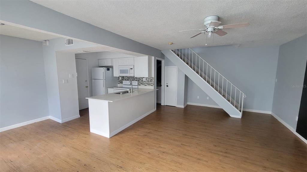 An open-concept kitchen with white cabinets and a breakfast bar overlooks a living area — 4410 SHADOW CREST PLACE UNIT 41-2, ORLANDO, FL