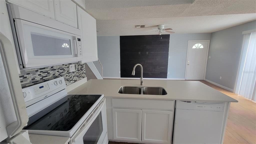 A kitchen with white cabinets, a light-colored countertop, and a dark wood accent wall — 4410 SHADOW CREST PLACE UNIT 41-2, ORLANDO, FL