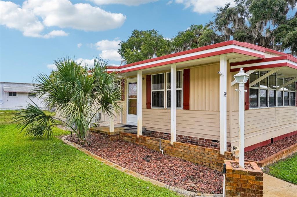A tan mobile home with red trim features a brick foundation and a palm tree — 29 HARBOR OAKS DRIVE, FRUITLAND PARK, FL
