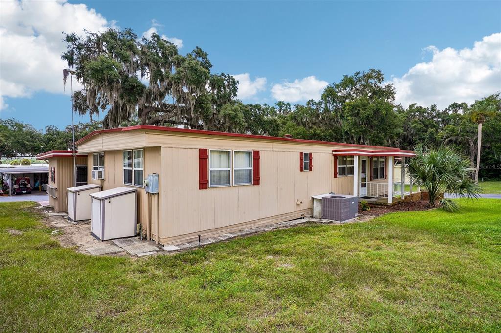 A tan mobile home with red trim and shutters sits on a grassy lot — 29 HARBOR OAKS DRIVE, FRUITLAND PARK, FL