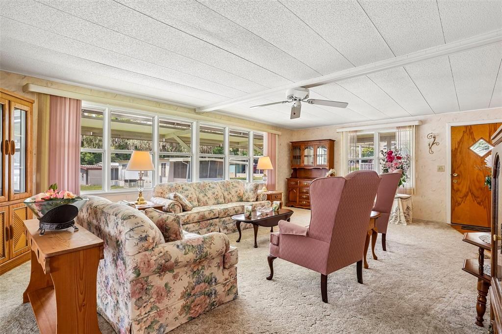 A living room features floral sofas, pink armchairs, a ceiling fan, and light-colored carpeting — 29 HARBOR OAKS DRIVE, FRUITLAND PARK, FL