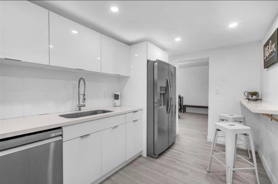 A modern kitchen features white flat-panel cabinets, stainless steel appliances, and a breakfast bar — 4001 S Ocean Drive # 7k, Hollywood FL 33019, HOLLYWOOD, FL