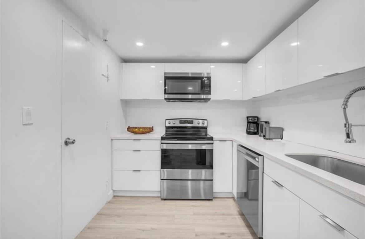 A modern kitchen features white high-gloss cabinets, stainless steel appliances, and light wood-look flooring — 4001 S Ocean Drive # 7k, Hollywood FL 33019, HOLLYWOOD, FL