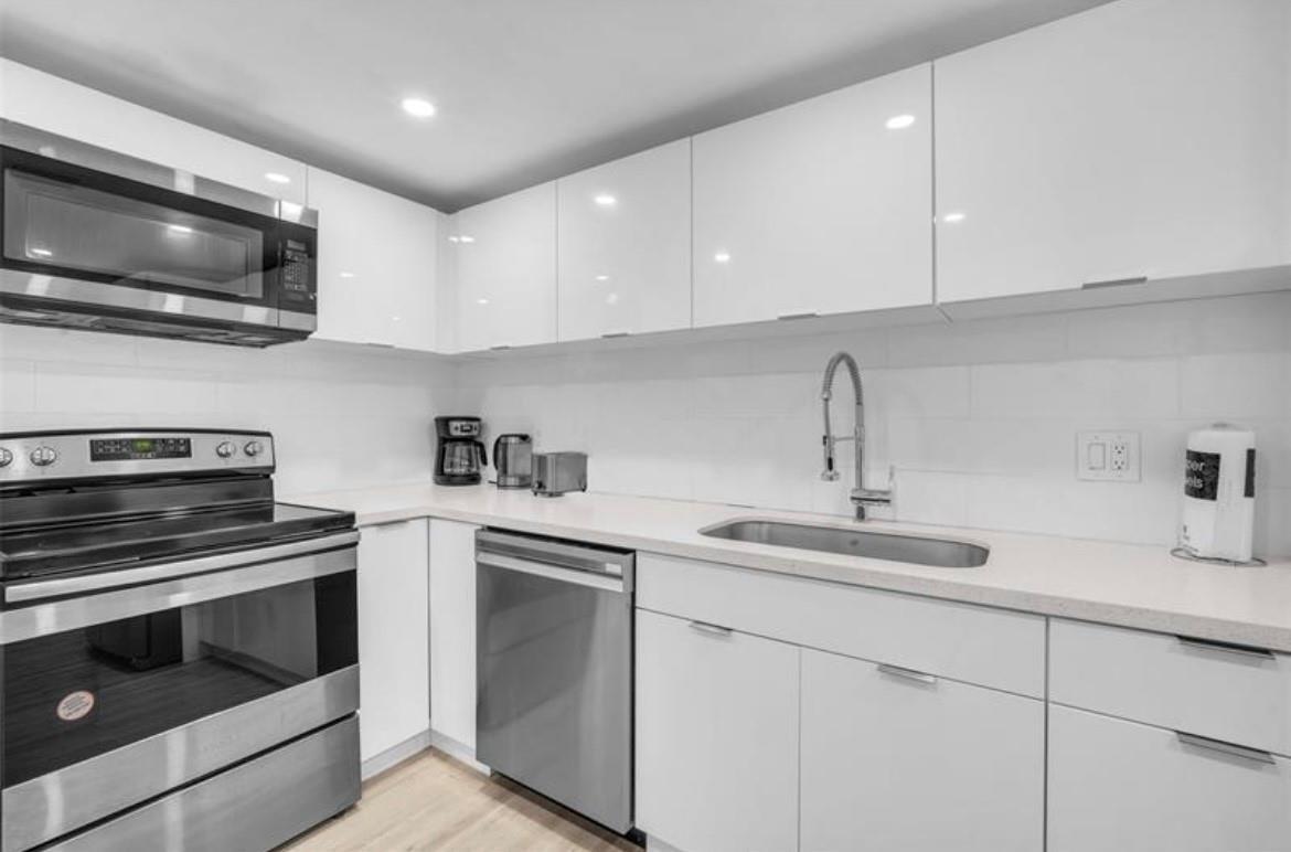 A modern kitchen features white glossy cabinets, stainless steel appliances, and white countertops — 4001 S Ocean Drive # 7k, Hollywood FL 33019, HOLLYWOOD, FL