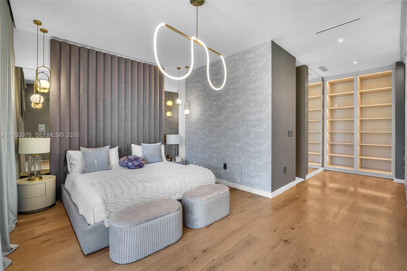 A modern bedroom features a tufted headboard, a unique light fixture, and built-in shelving — 46 NE 162nd St, Miami FL 33162, MIAMI, FL