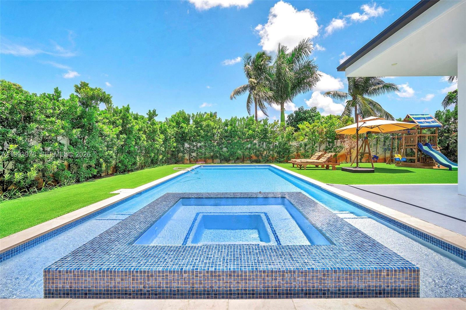 A rectangular swimming pool with an integrated spa sits in a backyard with artificial turf — 46 NE 162nd St, Miami FL 33162, MIAMI, FL