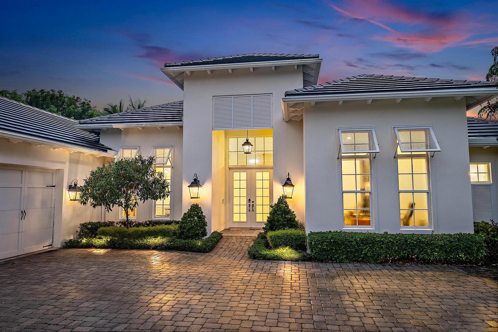 A modern white house with a paved driveway and illuminated entryway at dusk — 6081 Wildcat Run, West Palm Beach FL 33412, WEST PALM BEACH, FL