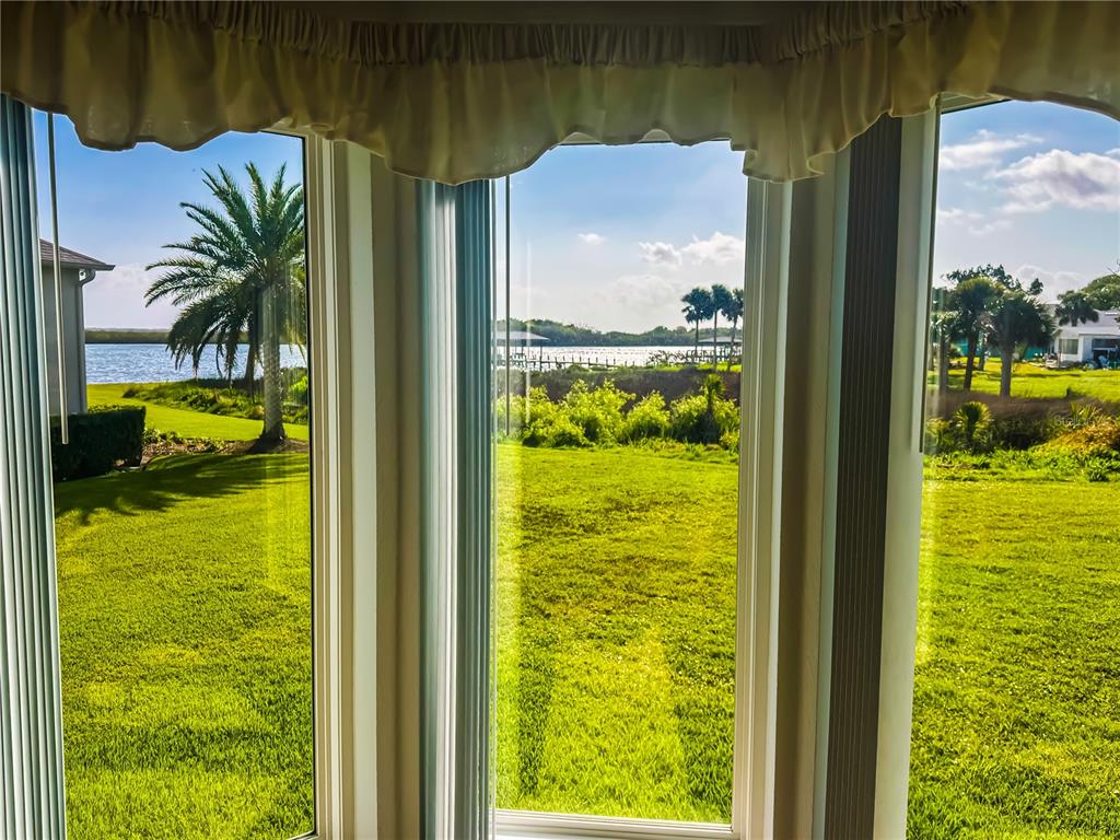 A view of a grassy lawn and water through a three-paneled bay window — 290 NAVAJO DRIVE, OAK HILL, FL