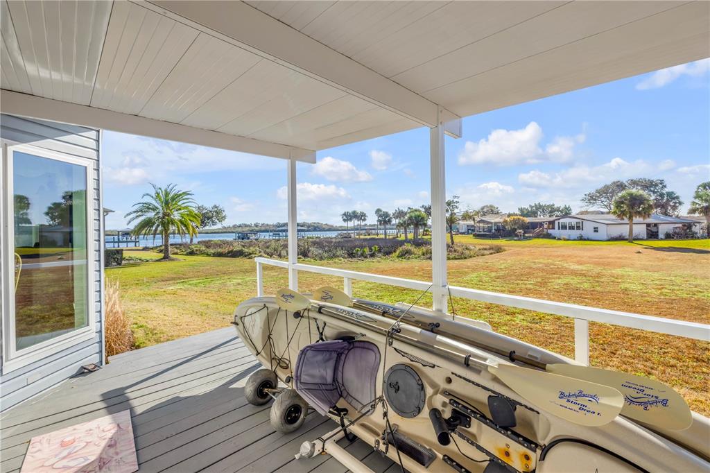 A covered wooden porch features a kayak on wheels overlooking a grassy yard and water — 290 NAVAJO DRIVE, OAK HILL, FL