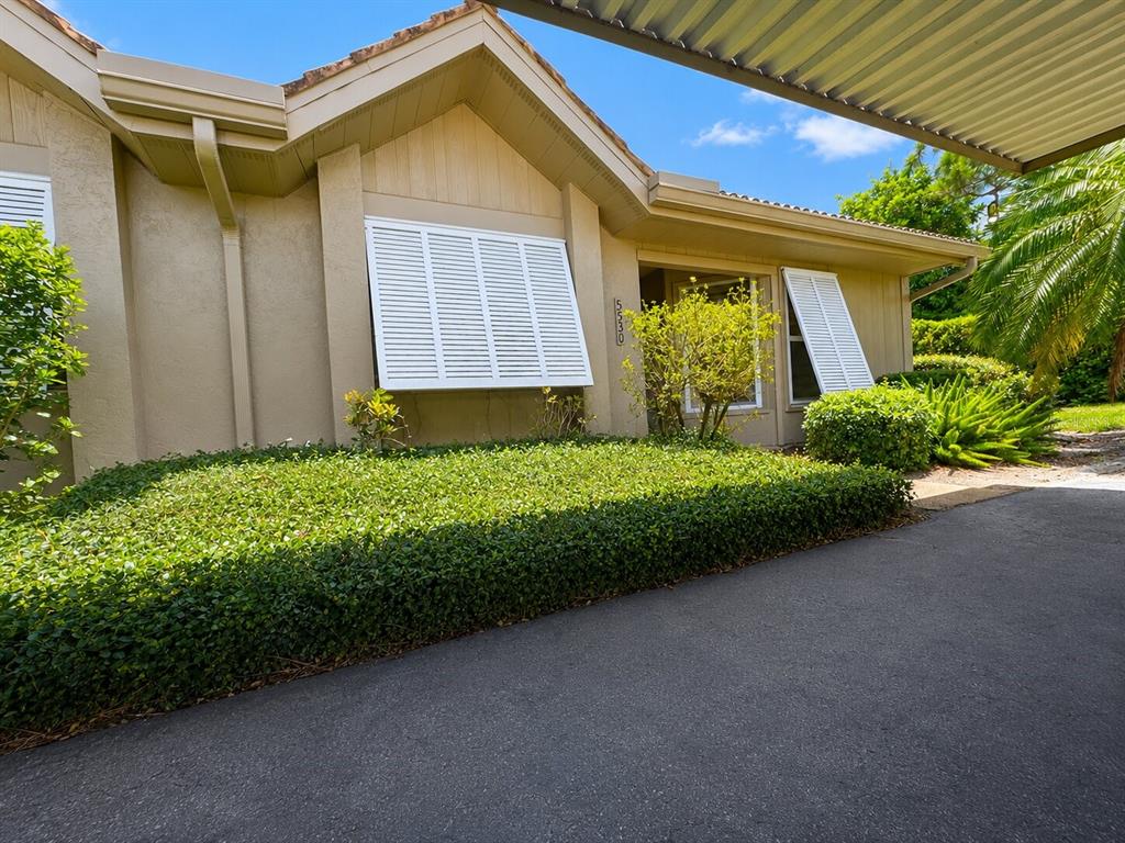 A tan house exterior features white shutters, a large hedge, and a covered driveway — 5530 37TH STREET E, BRADENTON, FL